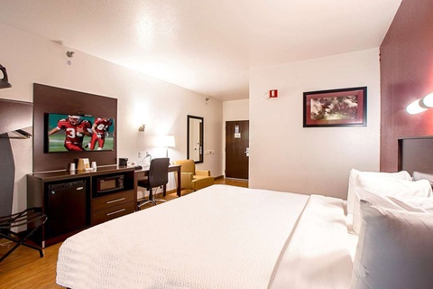A hotel room with a king-sized bed, desk, TV, and refrigerator.