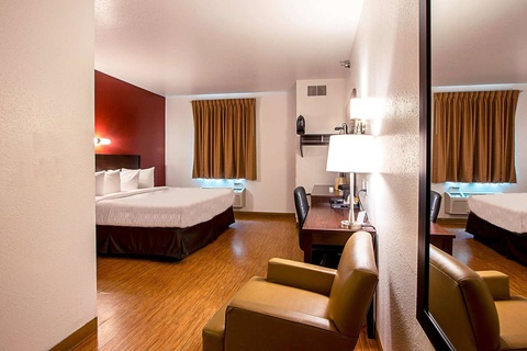 A hotel room with a bed, desk, chair, and mirror
