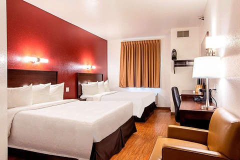 A hotel room with two queen beds, a desk, chair, and window with curtains.
