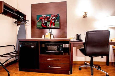 A hotel room with a desk, chair, TV, and mini-fridge.