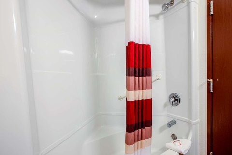 A bathroom shower with a red and white striped shower curtain, a white tub, and a soap dish.