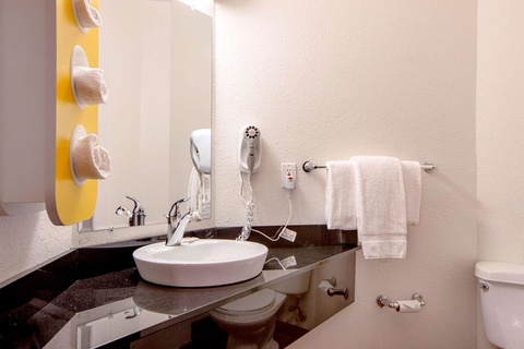 A clean bathroom with a white sink, toilet, and towels on a black countertop.