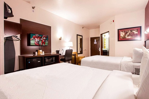 A hotel room with two queen beds, a TV, and a small desk.