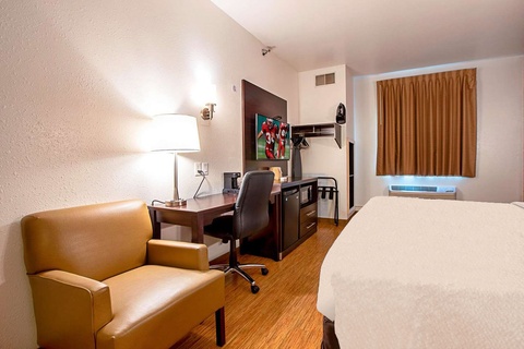 A hotel room with a king-sized bed, desk, chair, and lamp.