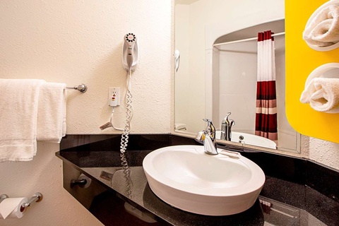 A bathroom sink with a white bowl and black countertop, with a mirror and towels nearby.