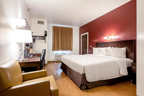 A hotel room with a bed, desk, chair, and lamp.